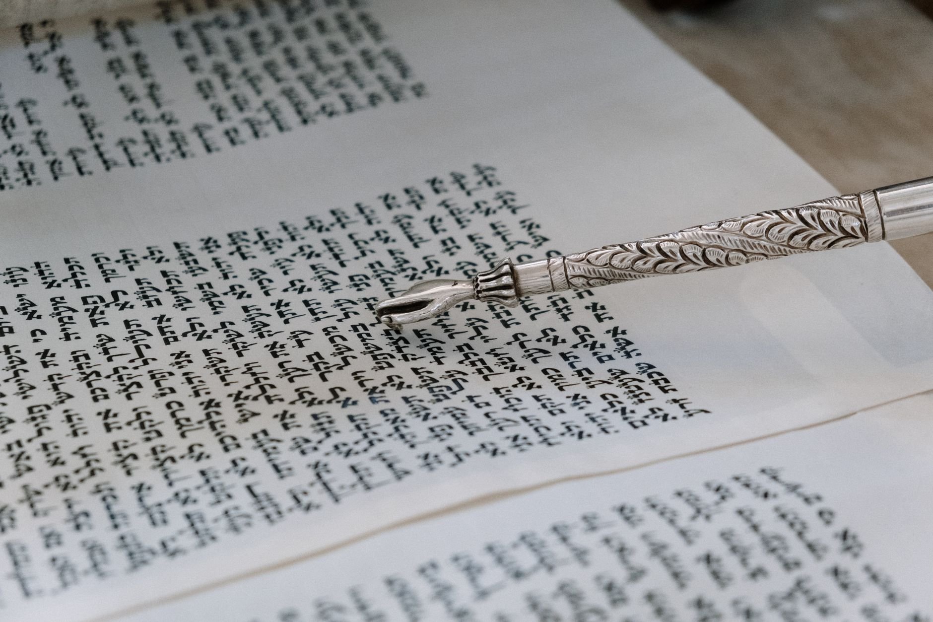 Silver yad pointing to Hebrew text in a Torah scroll